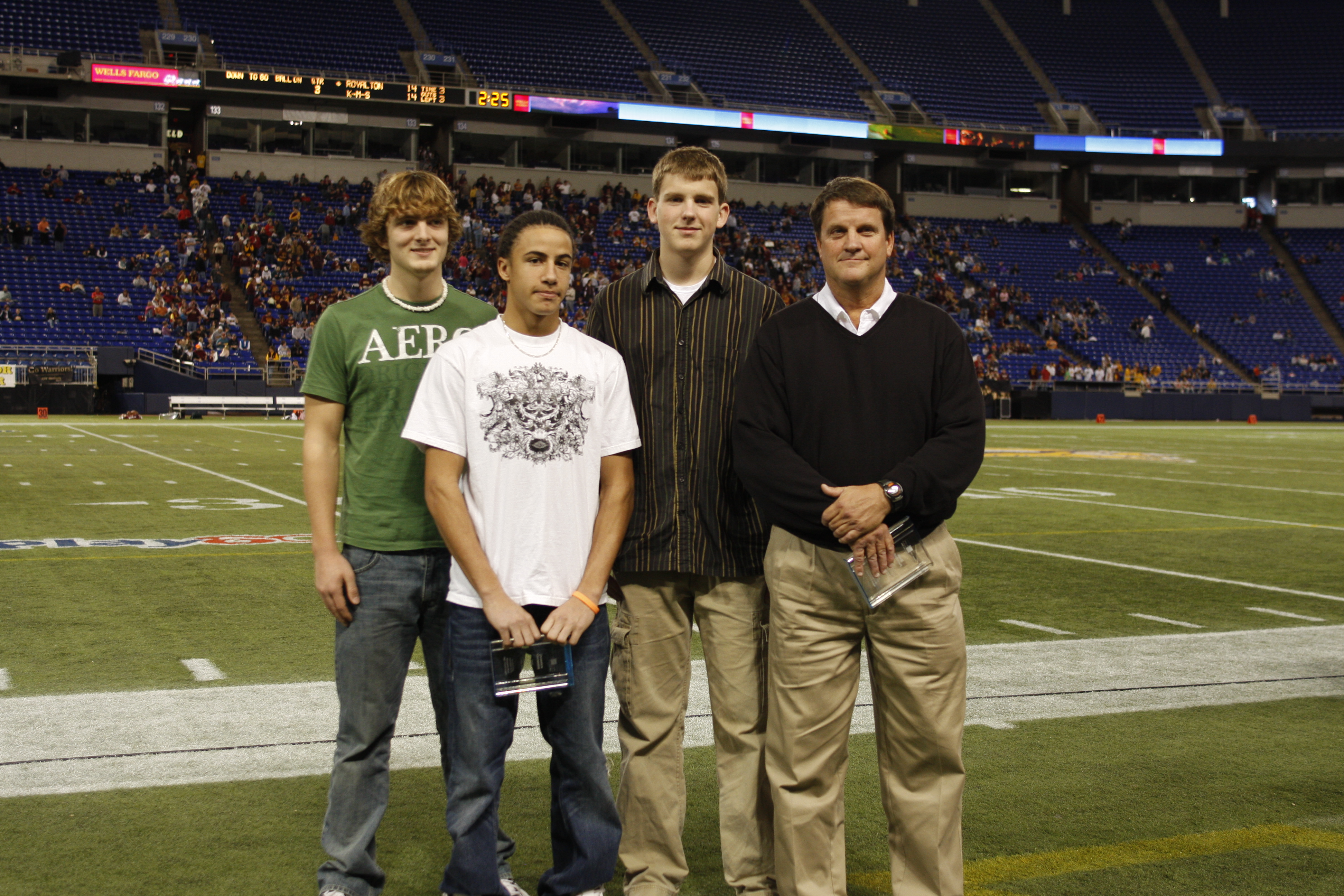 a student surrounded by two other students and the PE teacher who helped save his life